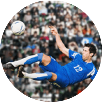 blue uniform clad soccer player kicking ball in mid air